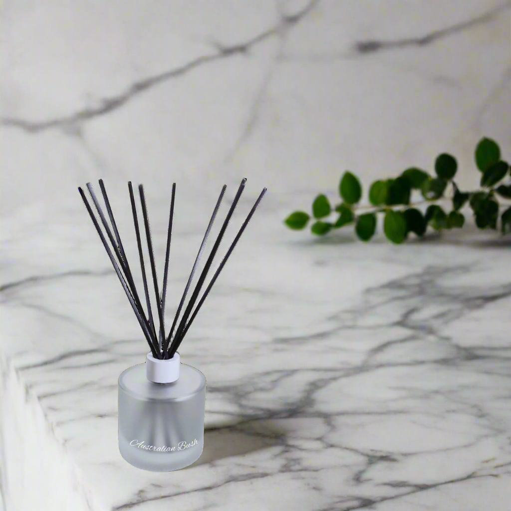 Reed diffuser with black sticks in a clear bottle on a marble surface