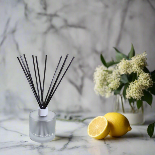 Reed diffuser with black sticks on a marble surface with lemons and flowers.