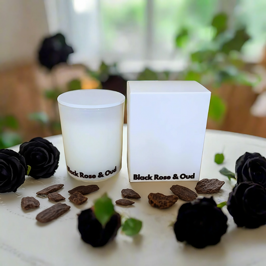 Candle and packaging labeled 'Black Rose & Oud' on a table with black roses.