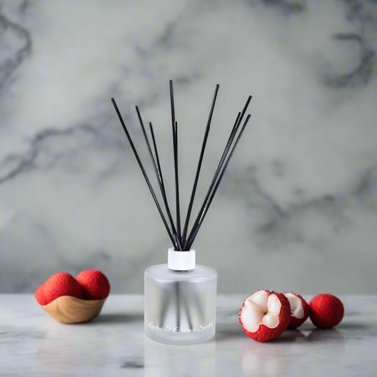 Reed diffuser with black sticks on a marble surface with red and white flowers.