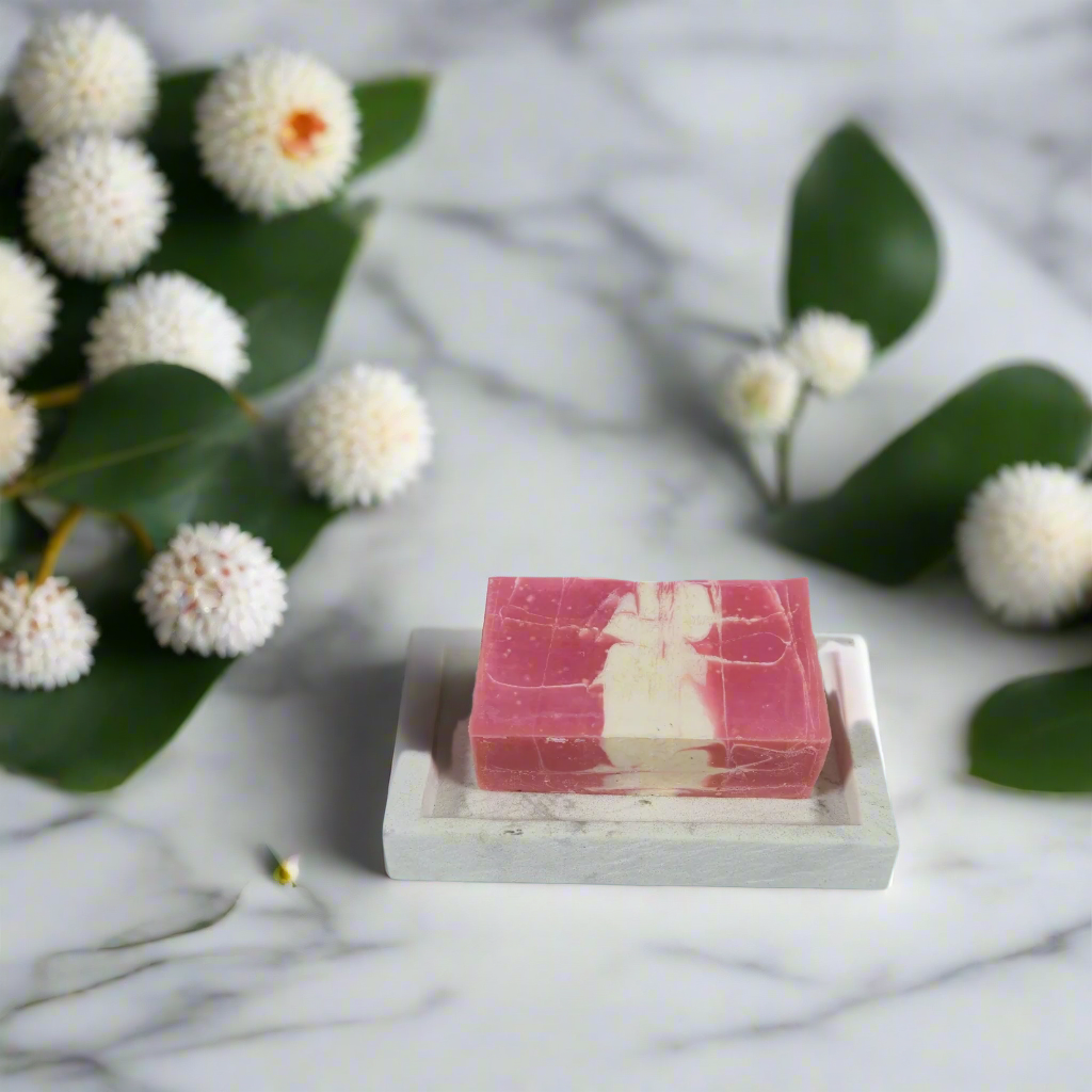 Pink and white striped soap bar on a marble surface with green leaves and white flowers.