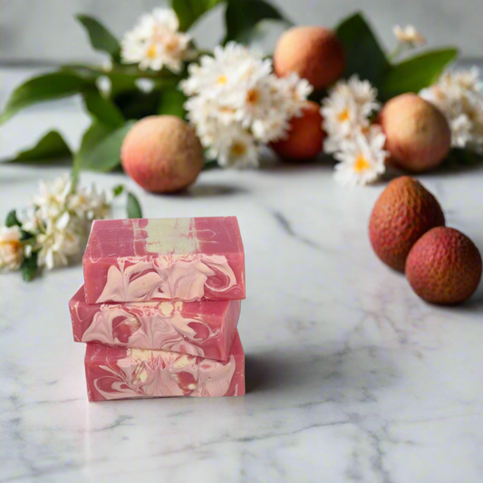 Stack of pink and white marbled soap bars with lychees and flowers on a marble surface