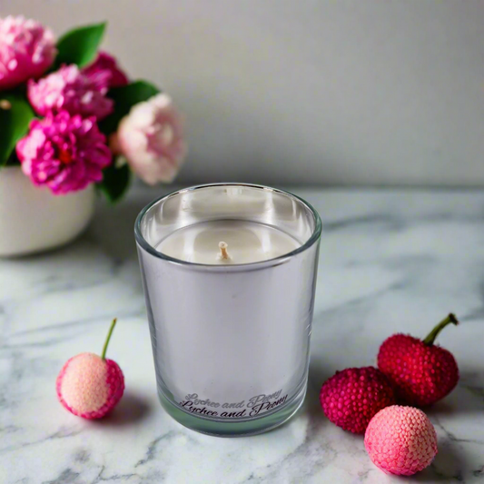 Candle in a glass jar on a marble surface with lychees and pink flowers in the background