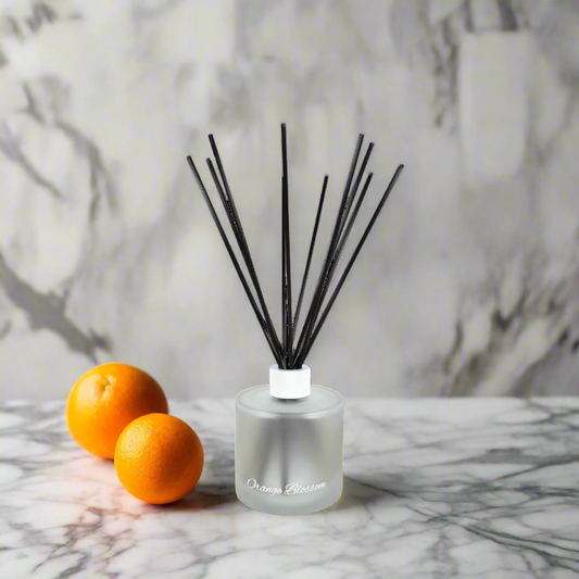 Reed diffuser with black sticks and a bottle cap on a marble surface with two oranges.