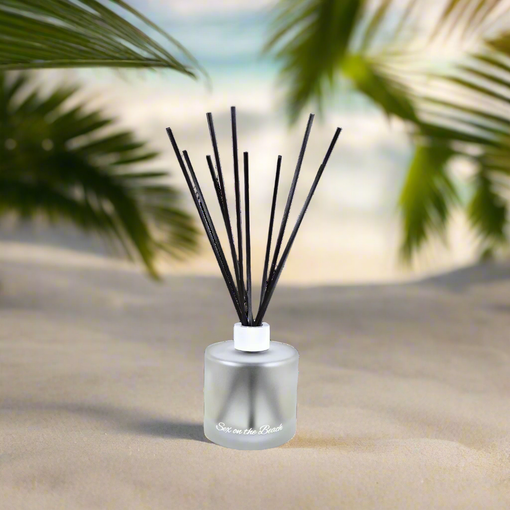 Diffuser with black sticks on a beach with palm leaves in the background