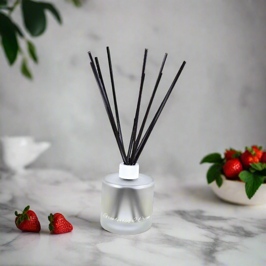 Silver diffuser with black sticks on a marble surface with strawberries and a plant in the background