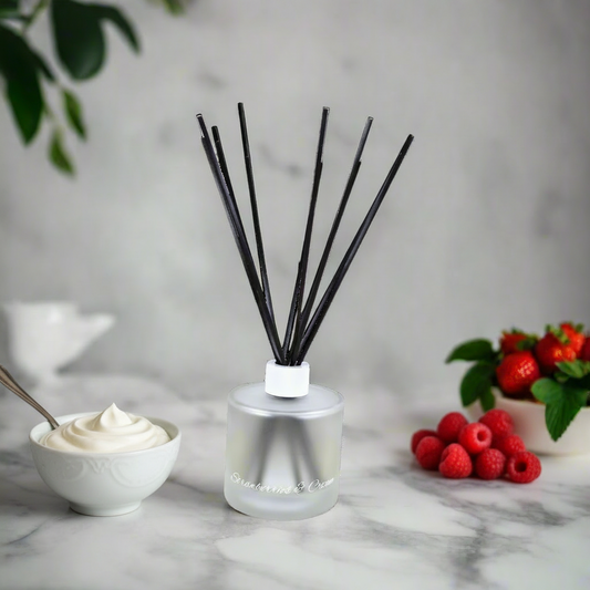 Silver diffuser with black sticks on a marble surface with strawberries and a plant in the background