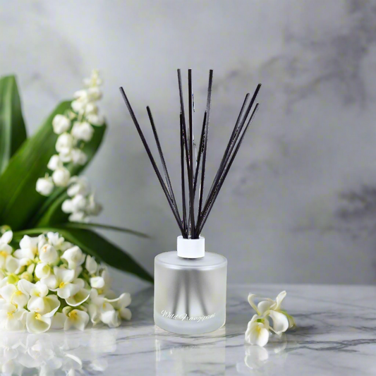 Reed diffuser with black sticks on a marble surface with white flowers.