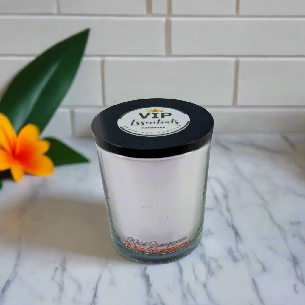 Glass candle with black lid on a marble surface with a flower and tiled wall in the background