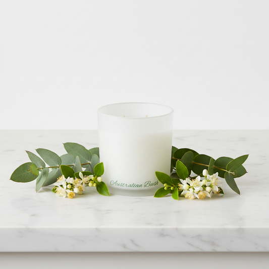 White candle with 'Australian Bush' branding on a marble surface with eucalyptus leaves and flowers.