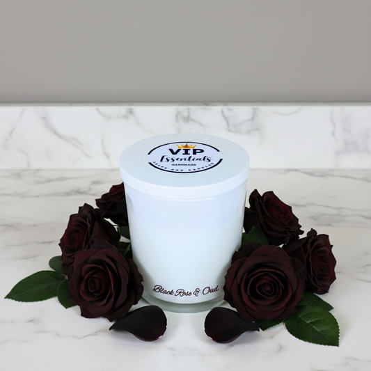 White candle with 'VIP Essentials' branding surrounded by dark red roses on a marble surface