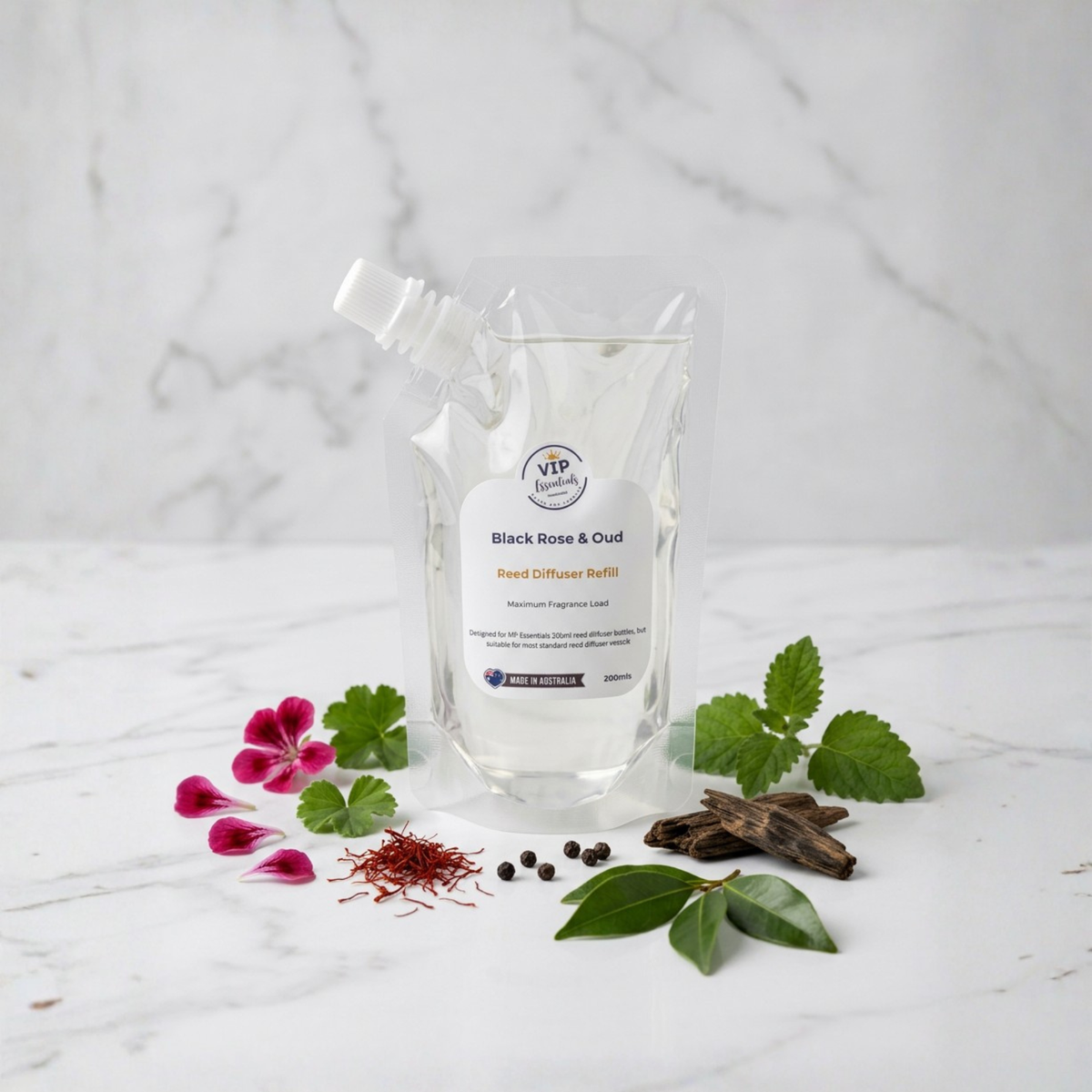 A clear stand-up pouch of V&P Vessels Black Rose & Oud Seed Diffuser Buffer with a white label, styled on a white marble surface with rose petals, green leaves, cinnamon, and saffron.