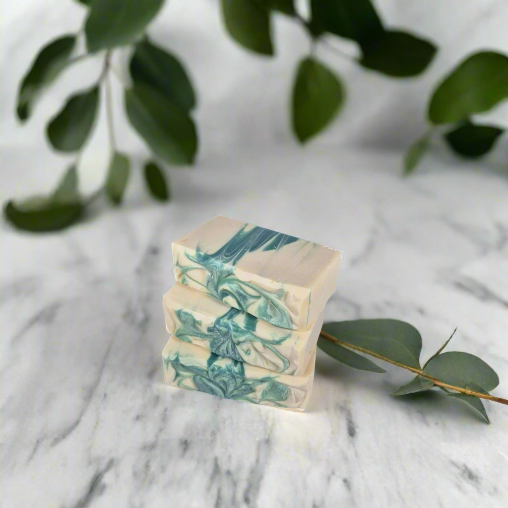 Three marbled soap bars stacked on a marble surface with green leaves in the background