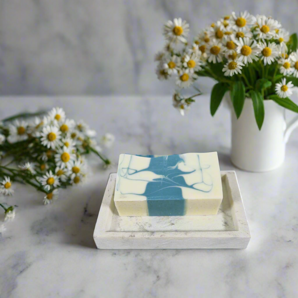 Bar of soap with a floral design on a marble tray with daisies in the background