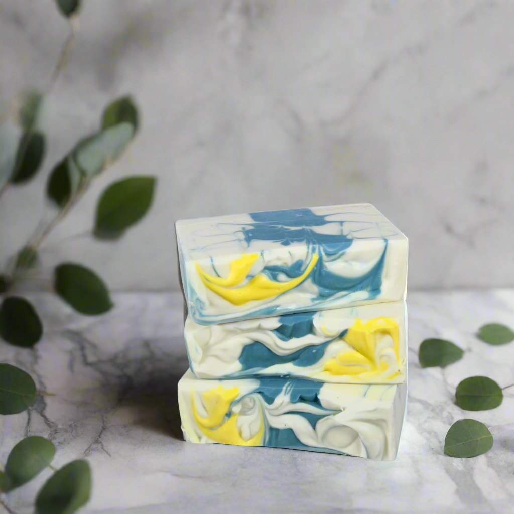 Two bars of soap with blue and yellow swirls on a marble surface with green leaves.