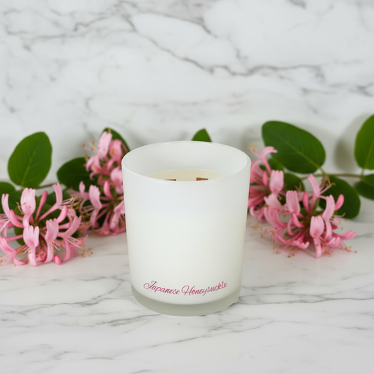 White candle with 'Japanese Honeysuckle' label on a marble surface with honeysuckle flowers.