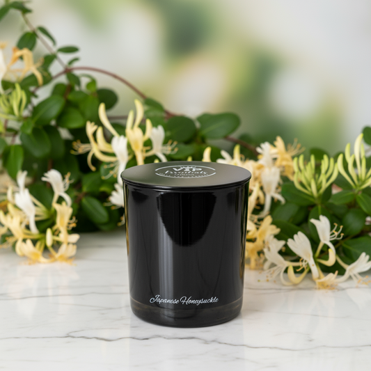 Black candle jar with 'Japonica Honeysuckle' text in front of honeysuckle flowers