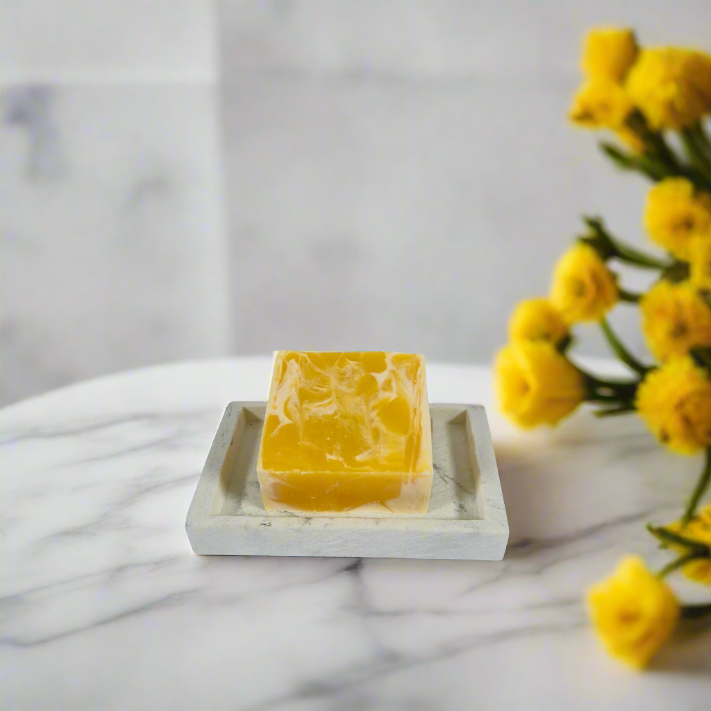 Yellow soap bar on a white marble surface with yellow flowers in the background