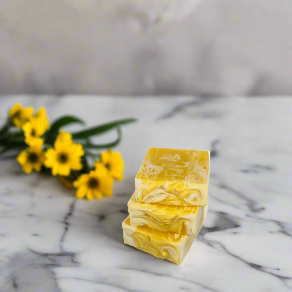 Three bars of yellow soap stacked on a marble surface with yellow flowers in the background.