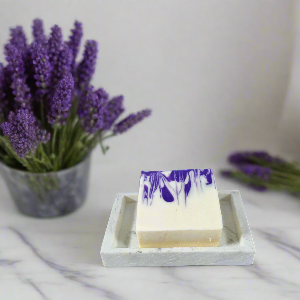 Bar of soap with purple and white swirls on a stone soap dish against a blue background