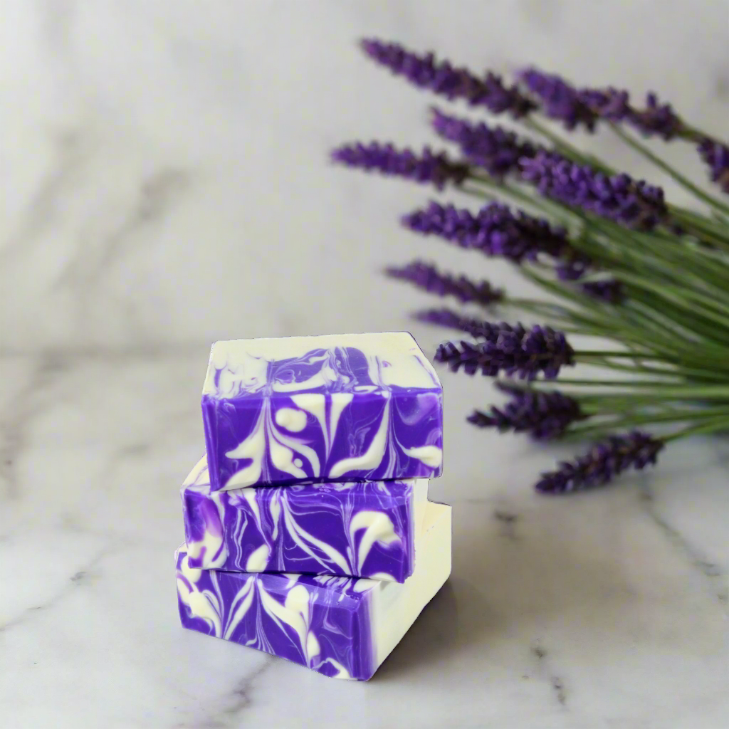 Three bars of purple and white marbled soap stacked on a marble surface with lavender flowers.