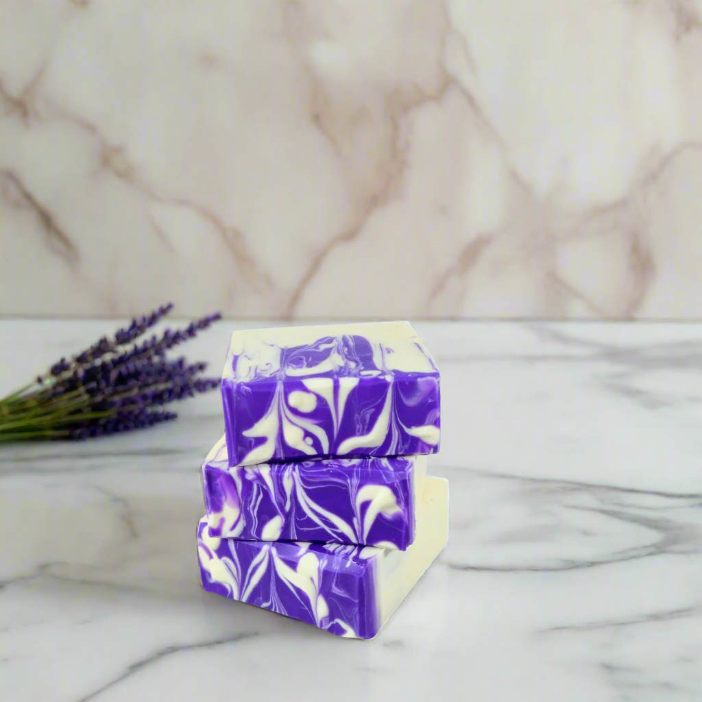 Two bars of purple and white marbled soap stacked on a marble surface with lavender flowers.