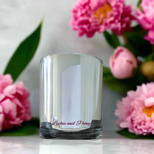 Clear glass candle holder with 'Lychee and Peony' text, surrounded by pink flowers.