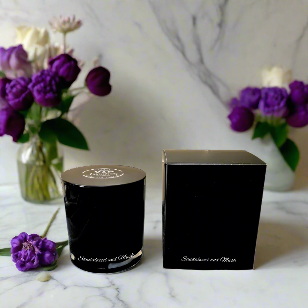 Black candle and box with 'Scented and Mask' branding on a marble surface with purple flowers.