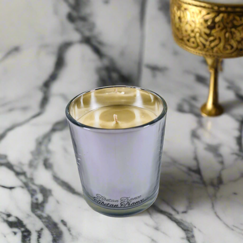 Candle in a glass holder on a marble surface with a gold decorative object in the background