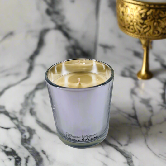 Candle in a glass holder on a marble surface with a gold decorative object in the background