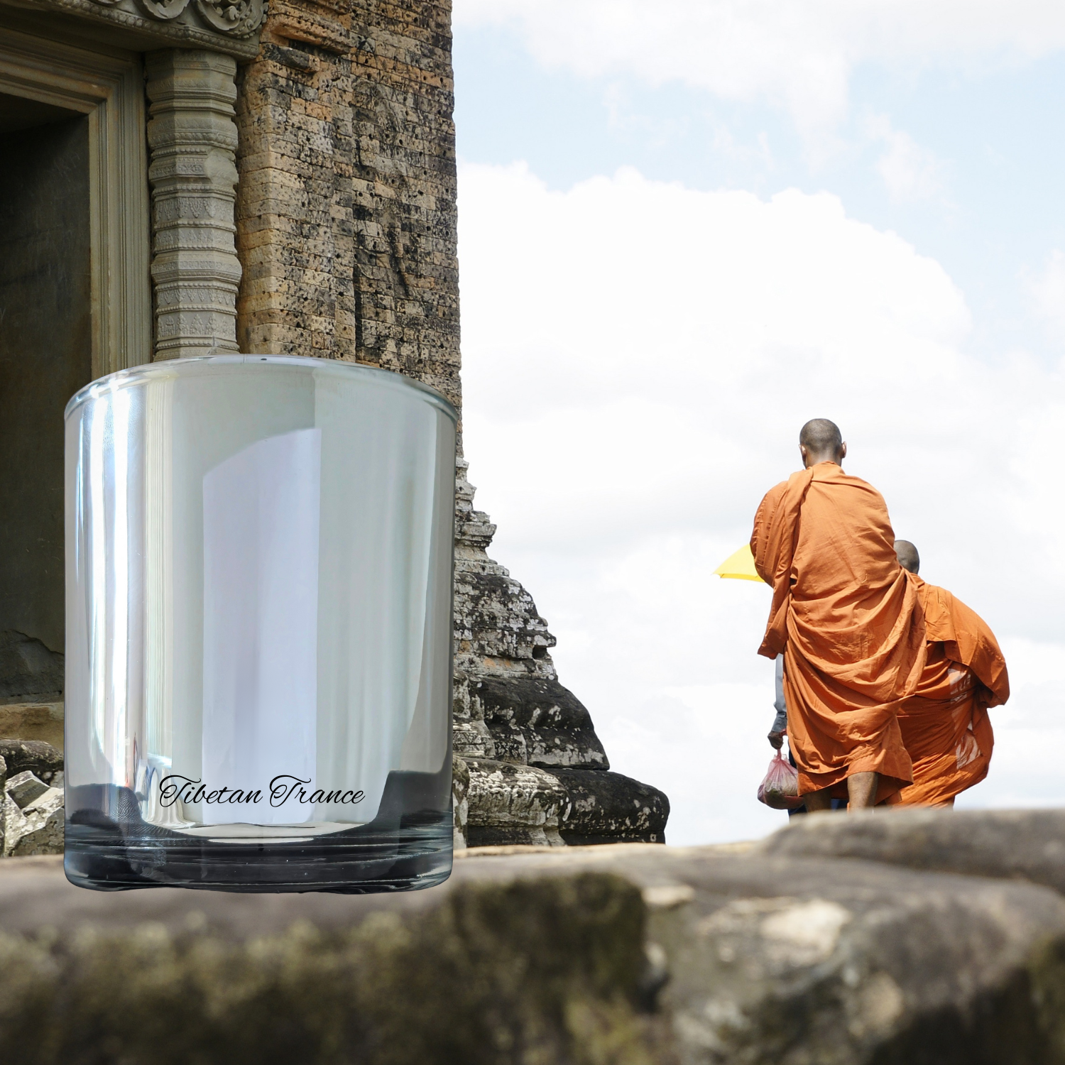 Monk in orange robes sitting on stone steps with a glass container labeled 'Aubertine France' in the foreground.