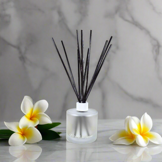 Reed diffuser with black sticks and a clear bottle on a marble surface with white flowers.